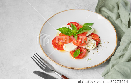 Caprese salad with sliced tomatoes, mozzarella and basil on a plate on a light background Caprese salad with sliced tomatoes, mozzarella and basil on a plate on a light background 125275914