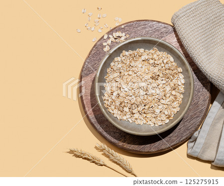 Oat flakes in bowl with wheat and napkin on a wooden board on a yellow background. 125275915