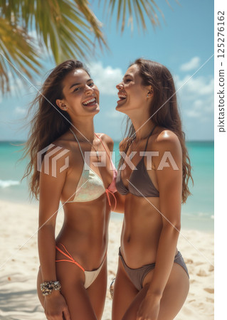 portrait of young beautiful girls wearing bikini swimsuit and posing on resort beach with view of sea and bright sky 125276162