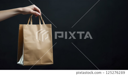 Brown paper shopping bag held by hand against black background with copy space Brown paper shopping bag held by hand against black background with copy space 125276289
