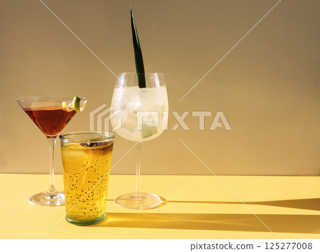 Close-up of three different delicious multicolored drinks. Glasses with tasty cocktails on a beige background. Fresh fruit drinks with ice. Sunlight. 125277008