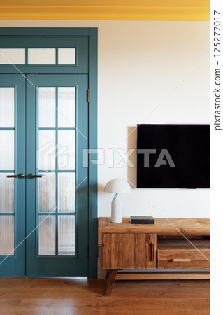 The elements of the stylish modern interior of the living room. Wooden chest of drawers with a lamp. Elegant blue glazed doors. The bright yellow ceiling. The elements of the stylish modern interior of the living room. Wooden chest of drawers with a lamp. Elegant blue glazed doors. The bright yellow ceiling. 125277017