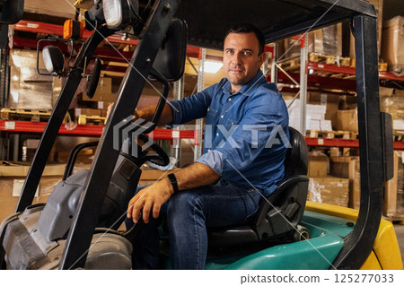 A young attractive forklift truck driver in a warehouse of goods. A handsome worker in casual clothes 125277033