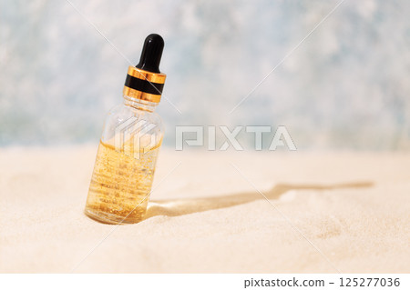 Mock-up of bottle of cosmetics with pipette and transparent liquid with gold particles on sand. Sunscreen essence with vitamins in glass tube. Mock-up of bottle of cosmetics with pipette and transparent liquid with gold particles on sand. Sunscreen essence with vitamins in glass tube. 125277036
