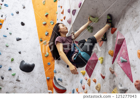 A young Asian woman on a climbing wall. A Korean girl climbs a bouldering wall 125277043