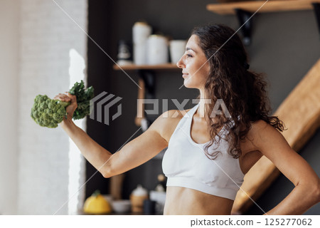 An attractive smiling vegan girl in a white top bites fresh broccoli. An attractive smiling vegan girl in a white top bites fresh broccoli. 125277062