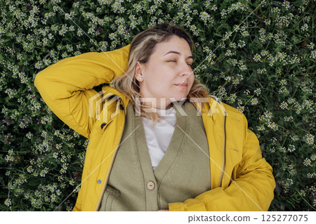 Top view of a charming young woman has closed her eyes and is lying on a blooming meadow. 125277075