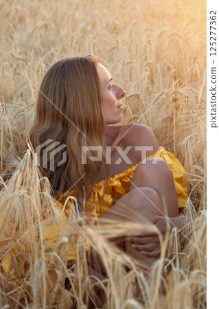 A girl with brown hair in a long yellow dress with a train in a wheat field at sunset. Posing model, fashion. High quality photo A girl with brown hair in a long yellow dress with a train in a wheat field at sunset. Posing model, fashion. High quality photo 125277362