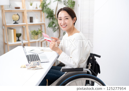Woman in wheelchair, money, bankbook, smile Woman in wheelchair, money, bankbook, smile 125277954