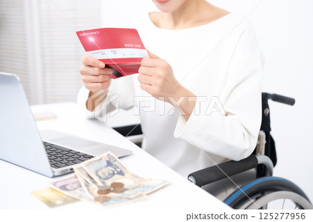Woman in wheelchair, money, bankbook, hand Woman in wheelchair, money, bankbook, hand 125277956