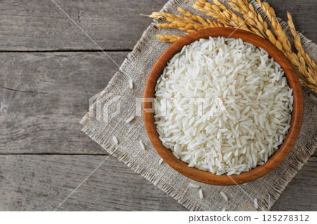 White rice filling wooden bowl on rustic table, complemented by delicate stalks White rice filling wooden bowl on rustic table, complemented by delicate stalks 125278312