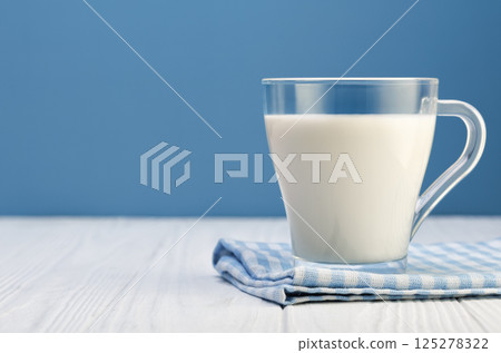 milk in glass cup resting on checkered cloth on white wooden table with blue background milk in glass cup resting on checkered cloth on white wooden table with blue background 125278322