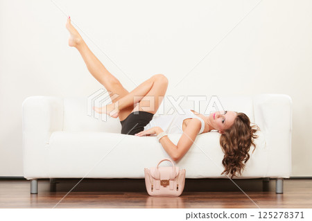 Fashionable girl with handbag lying on sofa 125278371