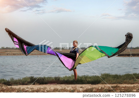 A woman with a multicolored parachute, an athlete riding kitersurfing on a blue pore. Beach, active recreation. Sunset competitions, parachute, board, freedom. High quality photo 125278896