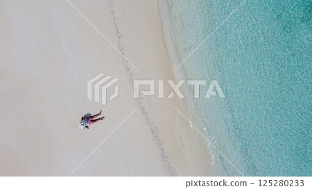 An aerial view of a young man in a white hat on the ocean shore 125280233
