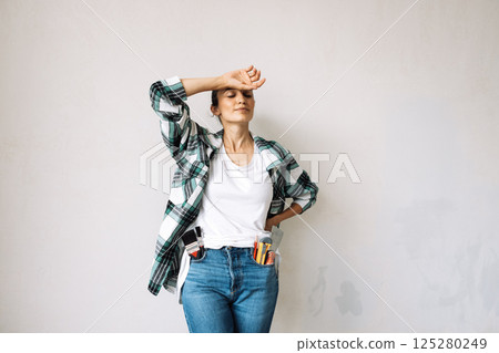 A tired young woman with construction tools in her jeans pockets in a renovated room. Renovation in an apartment or house. A tired young woman with construction tools in her jeans pockets in a renovated room. Renovation in an apartment or house. 125280249