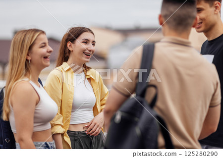 Four teenagers in casual clothes chat and laugh on the roof of the house Four teenagers in casual clothes chat and laugh on the roof of the house 125280290