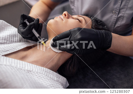 Beauty injections. Female cosmetologist in black gloves makes an injection in the lower jaw of her client Beauty injections. Female cosmetologist in black gloves makes an injection in the lower jaw of her client 125280307