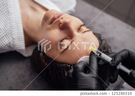 Female cosmetologist in transparent gloves makes an injection in the lower jaw of her client Female cosmetologist in transparent gloves makes an injection in the lower jaw of her client 125280310