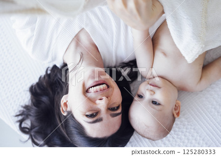 Pretty infant in a white bodysuit with his mom on a light background. Pretty infant in a white bodysuit with his mom on a light background. 125280333