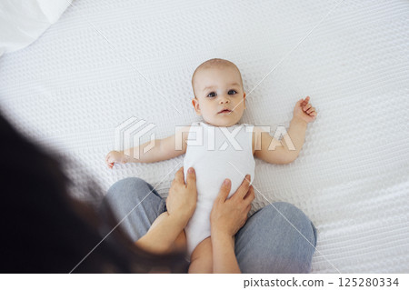 Pretty infant in a white bodysuit with his mom on a light background. Motherhood concept. 125280334