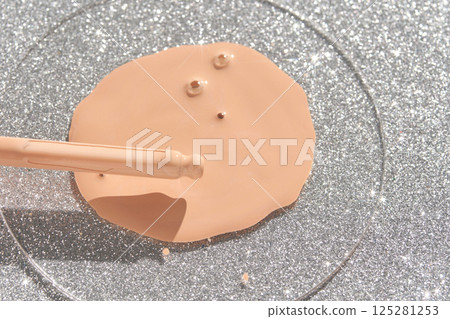 Beige liquid foundation spilled on glittery silver surface with applicator Beige liquid foundation spilled on glittery silver surface with applicator 125281253