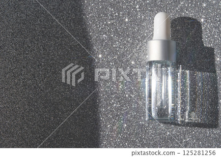 Transparent dropper bottle on glittery silver background with shimmering light Transparent dropper bottle on glittery silver background with shimmering light 125281256