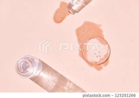 Abstract composition with glitter lip gloss tubes and spilled liquid on beige Abstract composition with glitter lip gloss tubes and spilled liquid on beige 125281266