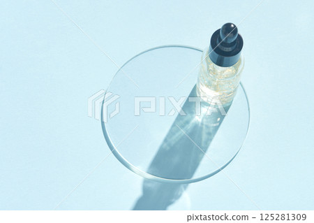 Minimalist skincare serum bottle with dropper casting shadow on light blue 125281309