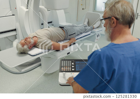 Male patient undergoing X-ray examination using tilting radiographic wall stand. Male patient undergoing X-ray examination using tilting radiographic wall stand. 125281330