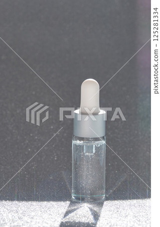 Transparent serum bottle with dropper on glittering surface in sunlight Transparent serum bottle with dropper on glittering surface in sunlight 125281334