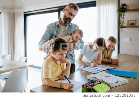 Father helping his daughters with homework while taking care of baby. 125281355