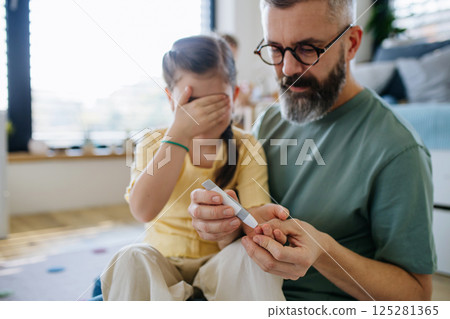 Father assisting his daughter with blood sugar test at home. 125281365
