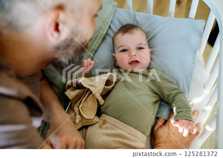 Father putting the baby to sleep, lying next to him in the crib. Father putting the baby to sleep, lying next to him in the crib. 125281372