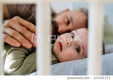 Father putting the baby to sleep, lying next to him in the crib. Father putting the baby to sleep, lying next to him in the crib. 125281373