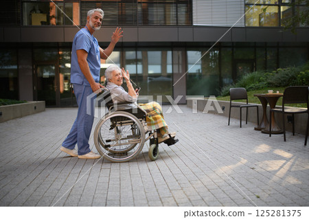 Male caregiver pushing senior woman in wheelchair. 125281375