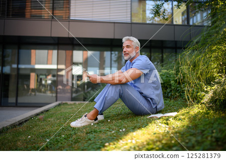 Healthcare worker resting in park outside hospital, holding smartphone. Healthcare worker resting in park outside hospital, holding smartphone. 125281379
