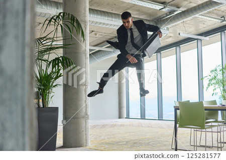 A businessman ecstatically jumping in a modern office, holding a briefcase in his hands, celebrating a moment of success and triumph. 125281577