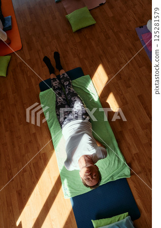 Senior woman practicing stretching and meditation on the floor, focusing on proper alignment and relaxation. 125281579