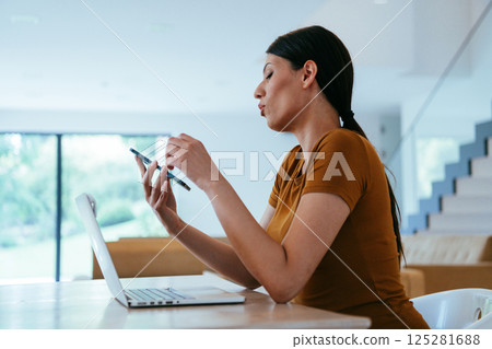 A woman sitting in the living room using a laptop and a smartphone look at camtalk by video call with business friends and relatives, head shot. Job interview answering questions.  125281688