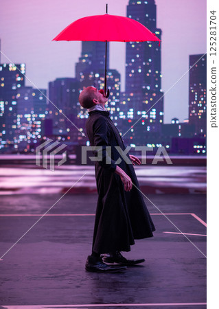 Mysterious Clown Performer with Red Umbrella in Urban Nightscape. Mysterious Clown Performer with Red Umbrella in Urban Nightscape. 125281704
