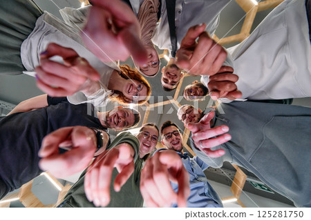 A group of cheerful young people gathered in a circle, pointing at the camera from a low-angle perspective. A group of cheerful young people gathered in a circle, pointing at the camera from a low-angle perspective. 125281750