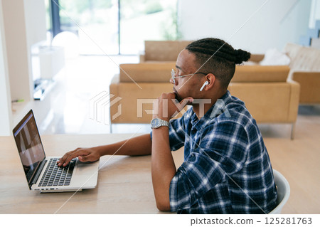 African American influencer in glasses sitting at a table in a modern living room, using a laptop for business video chat, conversation with friends and entertainment. 125281763