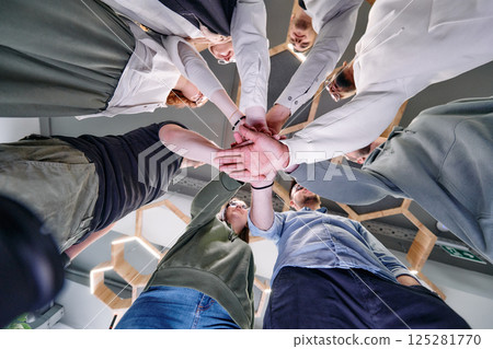 A group of young businessmen offer their hands together, symbolizing togetherness in the business world A group of young businessmen offer their hands together, symbolizing togetherness in the business world 125281770