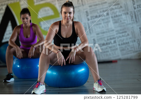 Two fitness women resting and recovering in the gym after an intense workout session, showcasing strength, endurance, and dedication to their fitness journey. Two fitness women resting and recovering in the gym after an intense workout session, showcasing strength, endurance, and dedication to their fitness journey. 125281799