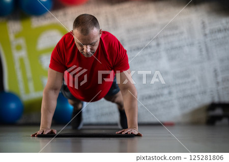 A muscular man performing push ups in the gym, showcasing strength, endurance, and dedication to his fitness routine. 125281806