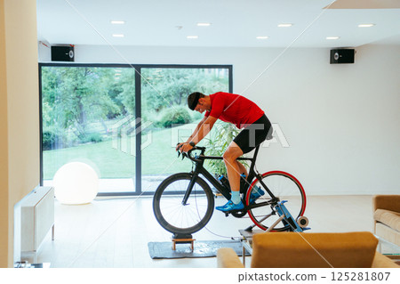 A triathlete riding a triathlon bike on a machine simulation in a modern living room 125281807