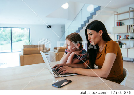Mother with her daughter talking on laptop with family and friends while sitting in modern living room of big house. Mother with her daughter talking on laptop with family and friends while sitting in modern living room of big house. 125281826