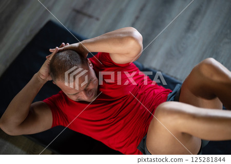 A muscular man performing crunches in the gym, focusing on building core strength and achieving his fitness goals 125281844