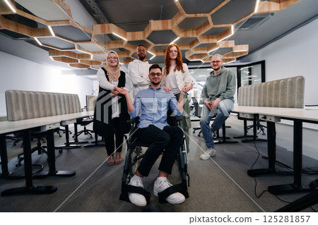 Young businessmen in a modern office extend a handshake to their business colleague in a wheelchair, showcasing inclusivity, support, and unity in the corporate environment. 125281857